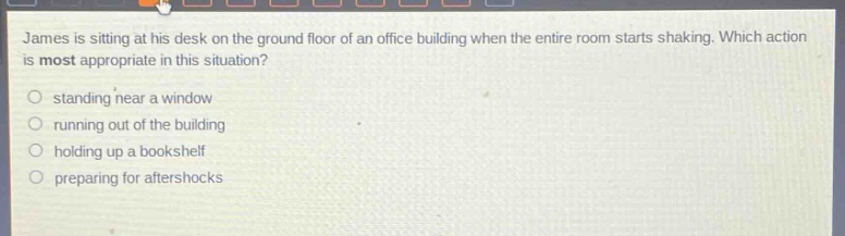 james is sitting at his desk on the ground floor of an office building when the entire room starts shaking. which action is most appropriate in this situation? standing near a window running out of the building holding up a bookshelf preparing for aftershocks