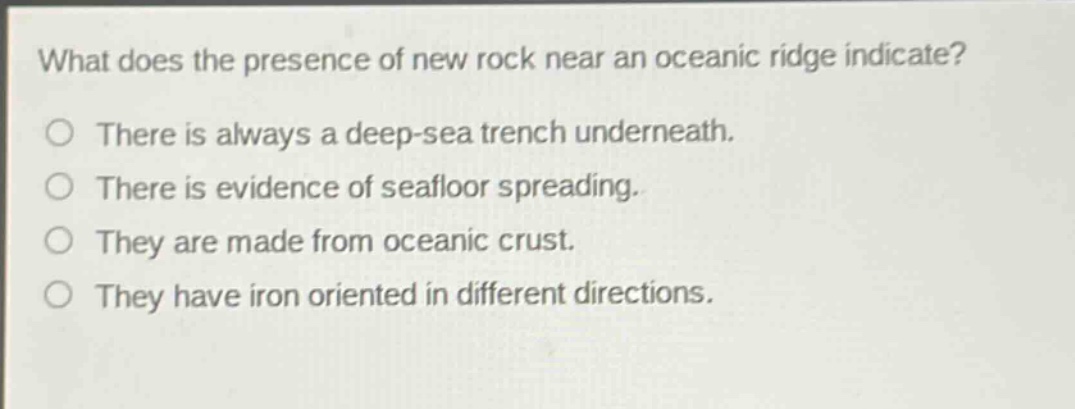 what does the presence of new rock near an oceanic ridge indicate?\nthere is always a deep - sea trench underneath.\nthere is evidence of seafloor spreading.\nthey are made from oceanic crust.\nthey have iron oriented in different directions.