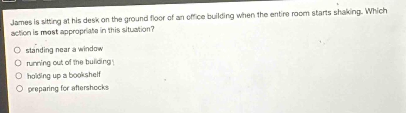 james is sitting at his desk on the ground floor of an office building when the entire room starts shaking. which action is most appropriate in this situation?\nstanding near a window\nrunning out of the building\nholding up a bookshelf\npreparing for aftershocks