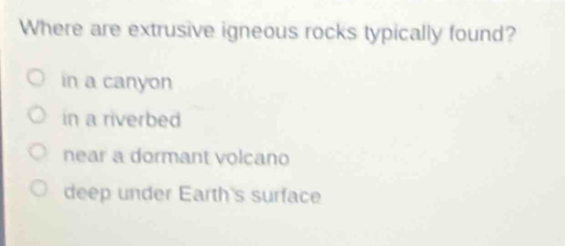 where are extrusive igneous rocks typically found?\n in a canyon\n in a riverbed\n near a dormant volcano\n deep under earths surface